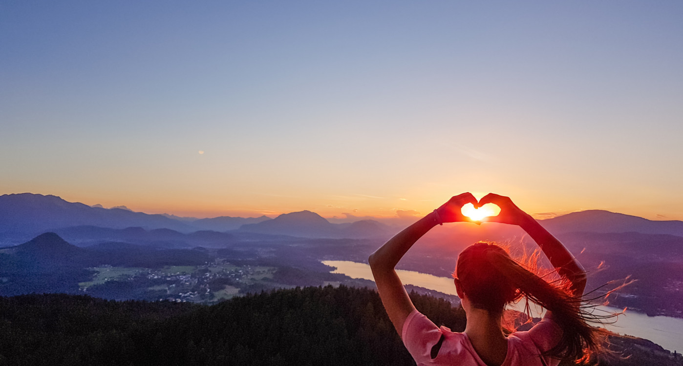 Frau formt mit den Händen ein Herz vor der untergehenden Sonne