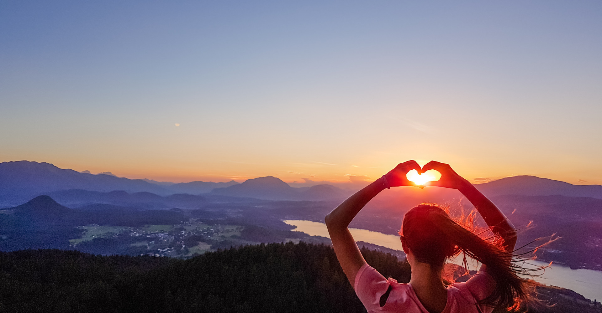 Frau formt mit den Händen ein Herz vor der untergehenden Sonne