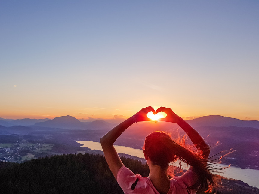 Frau formt mit den Händen ein Herz vor der untergehenden Sonne