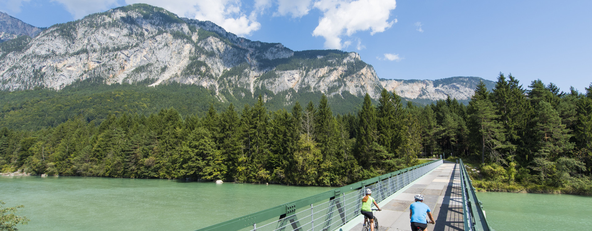 Zwei Radfahrer:innen beim Überqueren einer Brücke am Gail Radweg mit Blick auf den Dobratsch